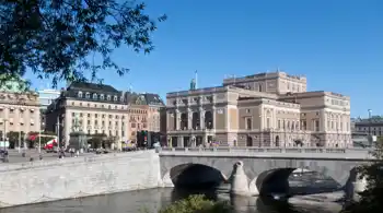 Large buildings against a blue sky, in the foreground a stream of water.