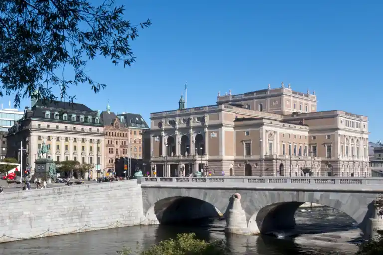 Large buildings against a blue sky, in the foreground a stream of water.