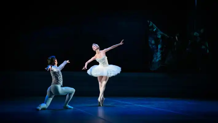 Two dancers on a dark stage: a man is kneeling and a ballerina is standing on tiptoe, wearing a tutu.