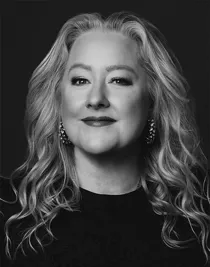 En närbild på en blond kvinna klädd i mörk tröja och med stora örhängen.