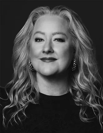 En närbild på en blond kvinna klädd i mörk tröja och med stora örhängen.