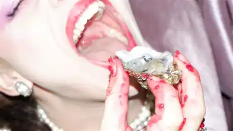 Närbild på en kvinna med kladdiga händer som för ett ostron mot sin mun.