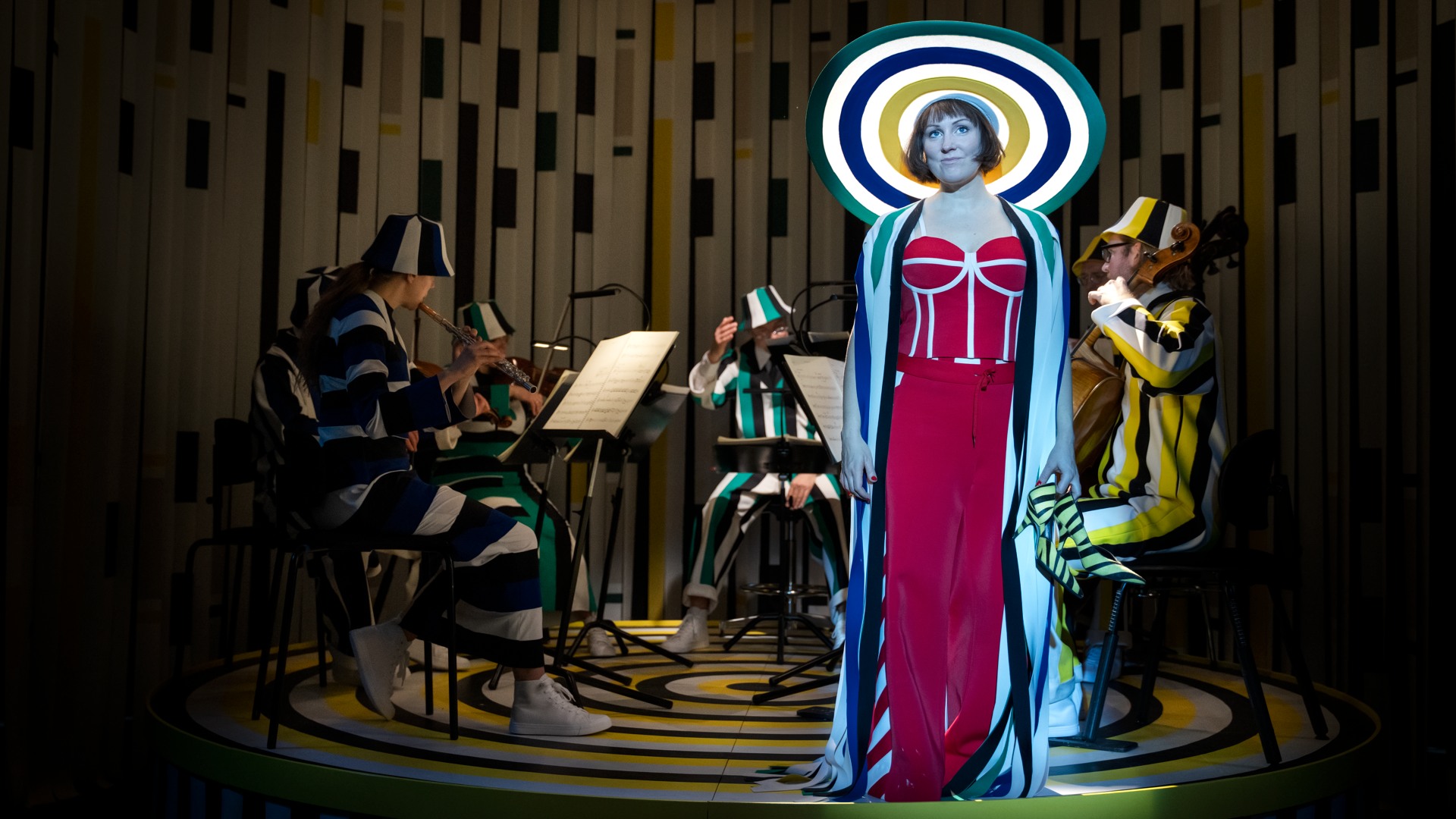En kvinna med en stor hatt står framför en orkester och tittar ut i fjärran.