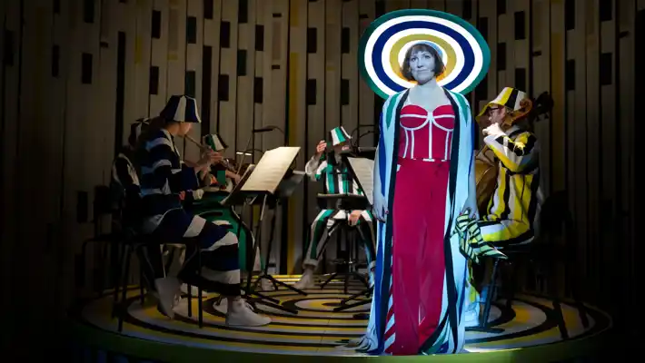 En kvinna med en stor hatt står framför en orkester och tittar ut i fjärran.