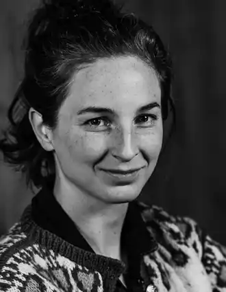 En närbild på en kvinna med mörkt hår: hon bär en mönstrad stickad kofta.