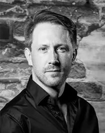 En närbild på en man i mörk skjorta som står mot en tegelvägg.