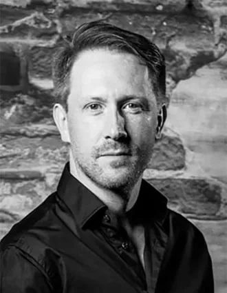 En närbild på en man i mörk skjorta som står mot en tegelvägg.