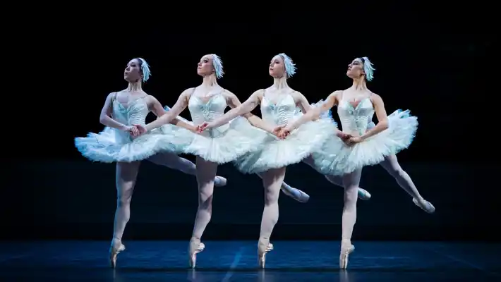 Four dancers wearing white tutus, all standing on tiptoe at the same time.