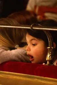 Person with blond hair rests his head on the ledge in a theater - a second person looks open-mouthed towards the stage.