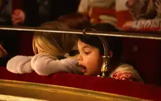 Person med blont hår vilar huvudet på kanten i en teatersalong - en andra person tittar med öppen mun mot scenen.