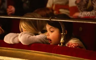 Person med blont hår vilar huvudet på kanten i en teatersalong - en andra person tittar med öppen mun mot scenen.