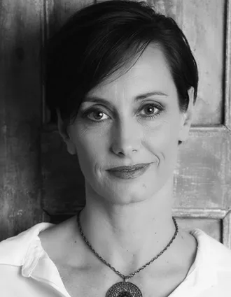 En närbild på en kvinna med mörkt kort hår, hon bär en vit skjorta och har ett stort halssmycke.