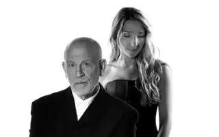 En man i kostym, bakom honom står en kvinna med långt hår.