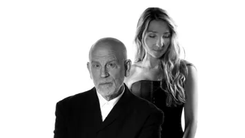 En man i kostym, bakom honom står en kvinna med långt hår.