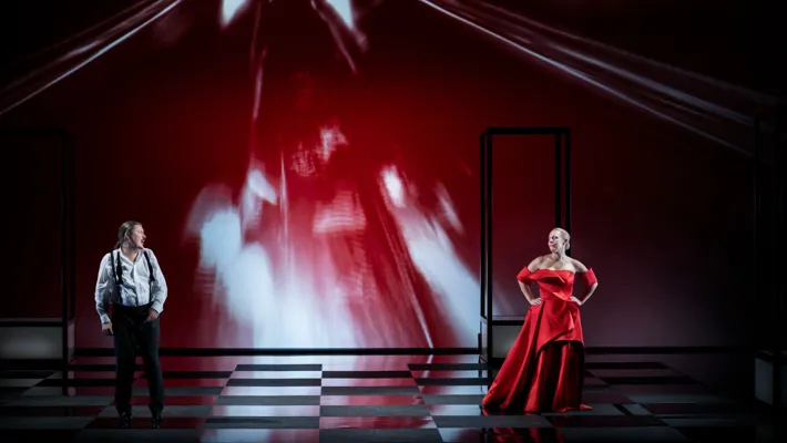 A woman in a magnificent red dress, in the background a man.