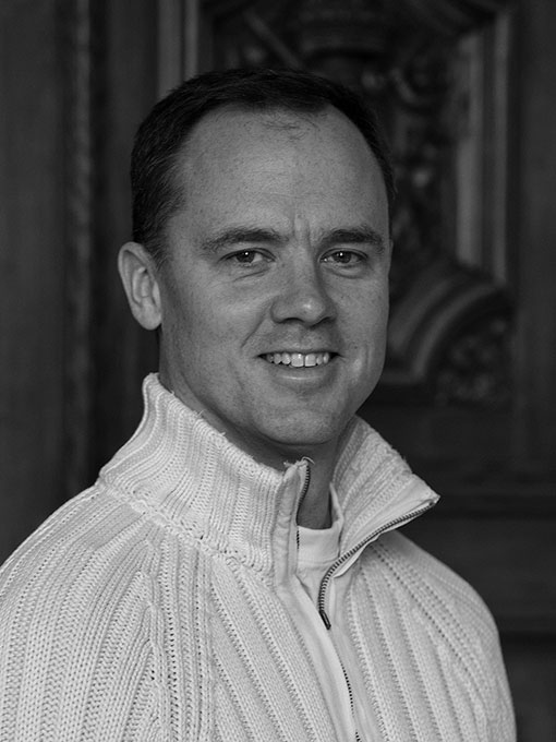 A close-up of a smiling man wearing a light knitted sweater.