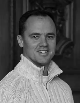 A close-up of a smiling man wearing a light knitted sweater.