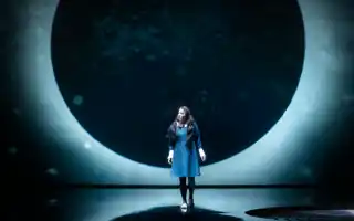 En månförmörkelse som fondkuliss, framför den står en kvinna i mörk klänning.