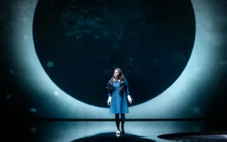 A lunar eclipse as a backdrop, in front of it stands a woman in a dark dress.