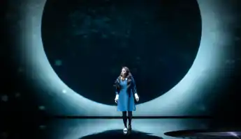 En månförmörkelse som fondkuliss, framför den står en kvinna i mörk klänning.