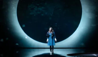 A lunar eclipse as a backdrop, in front of it stands a woman in a dark dress.