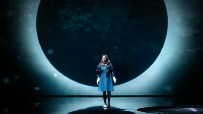 A lunar eclipse as a backdrop, in front of it stands a woman in a dark dress.