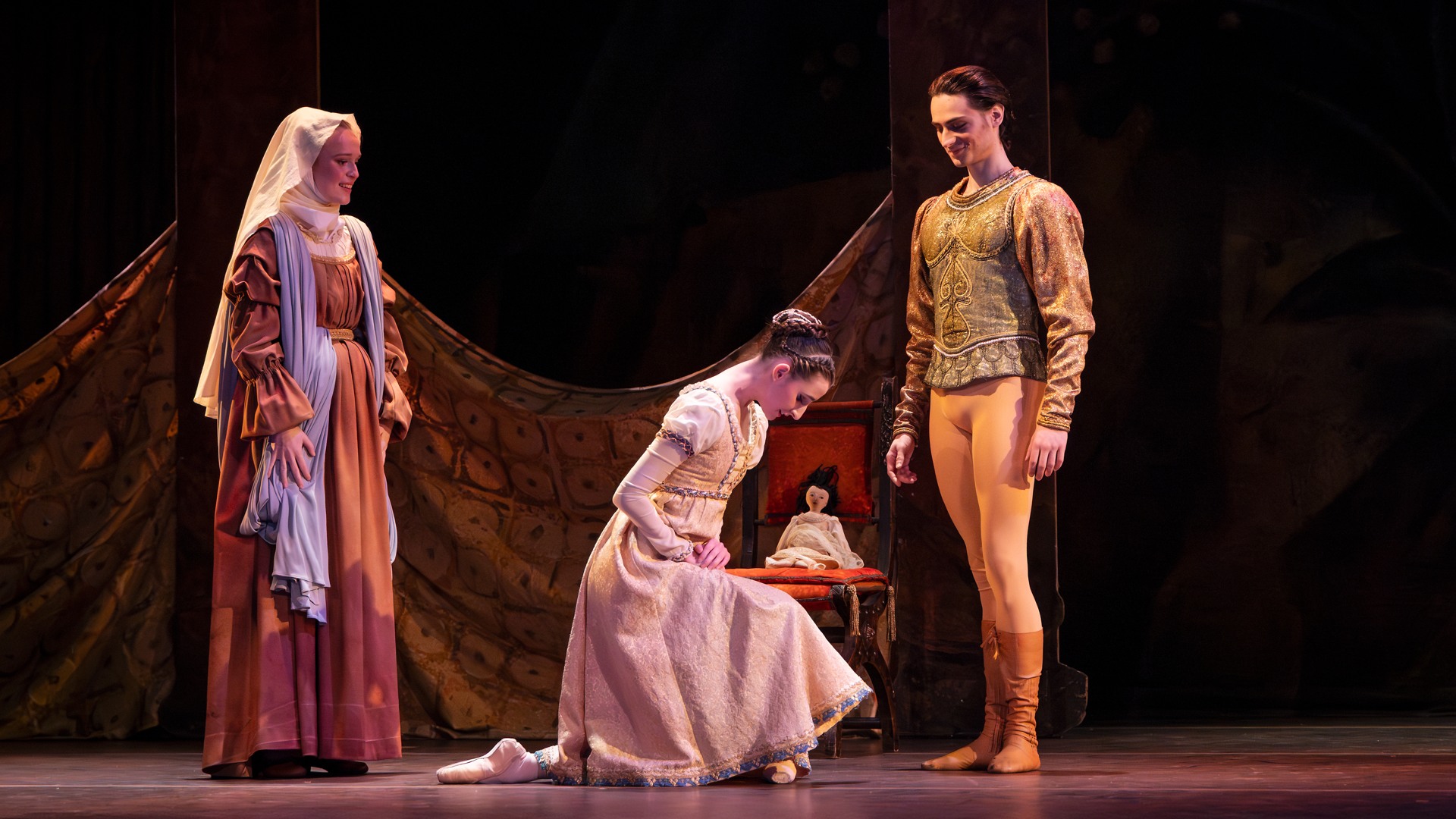 En kvinna knäböjer inför en man, bakom står en annan kvinna som verkar äldre.