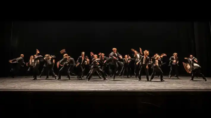 En stor mängd dansare rör sig energiskt på en scen.