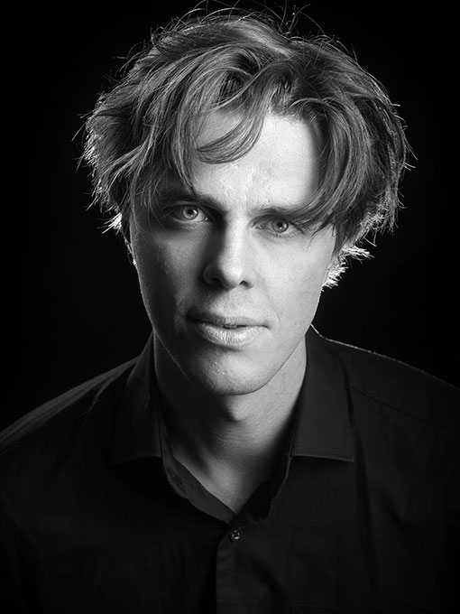 Close-up of a man with messy hair and a dark shirt.
