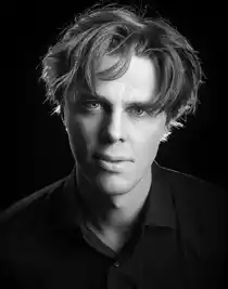 Närbild på en man med rufsigt hår och mörk skjorta.