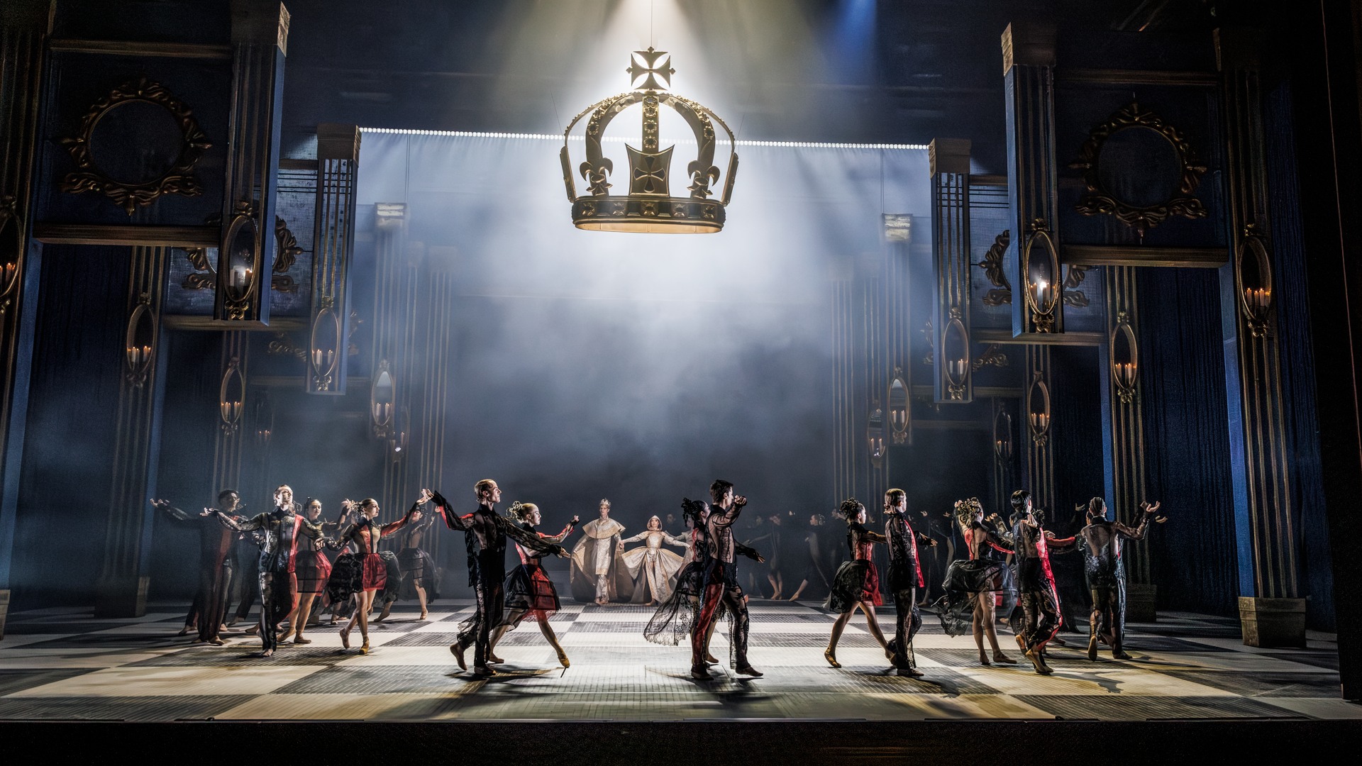 En scenbild med dekor som lyfter från golvet, en krona svävar över dansarna som rör sig i en ring.