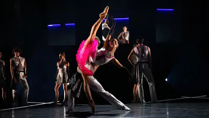 Två dansare utför ett komplext steg tillsammans, bakom flera andra dansare.