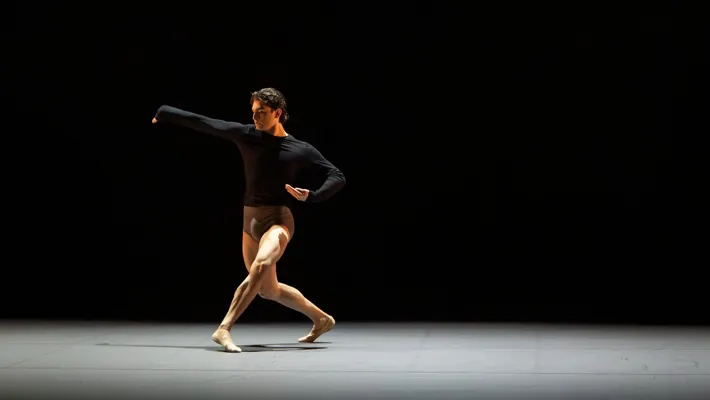 A lone dancer moves across a monochrome stage space.