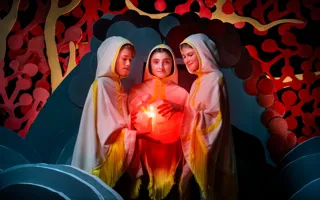 Tre barn i kåpor håller i ett runt föremål som lyser inifrån.