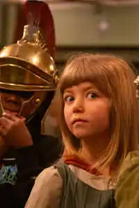 Two people in Roman helmets, their faces hidden, between them a girl with a surprised expression.