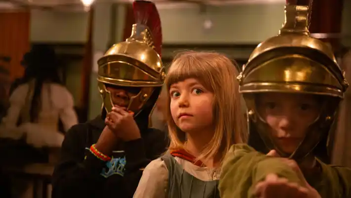 Two people in Roman helmets, their faces hidden, between them a girl with a surprised expression.