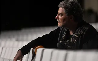A man in profile resting his arms against the backs of chairs.