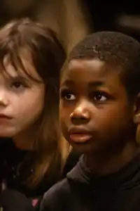 A photo of children in an indoor environment. The children wear colorful clothes and seem engaged in an activity.