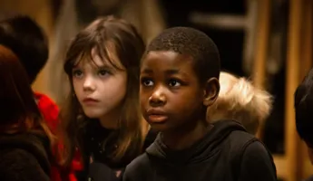 Ett foto av barn i en inomhusmiljö. Barnen bär färgglada kläder och verkar engagerade i en aktivitet.