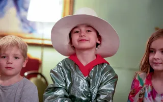 Tre yngre barn på rad, barnet i mitten har hatt och är utklädd.