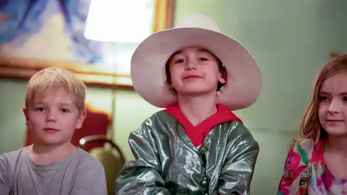 Tre yngre barn på rad, barnet i mitten har hatt och är utklädd.