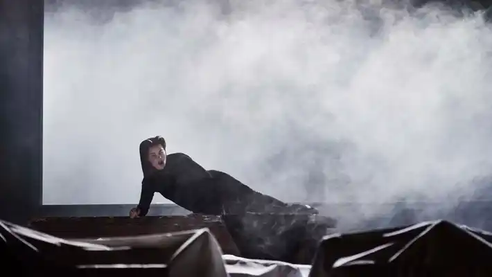 En mörkklädd kvinna halvligger på golvet om given av rök.