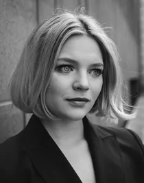 A close-up of a blonde woman wearing an elegant black jacket.
