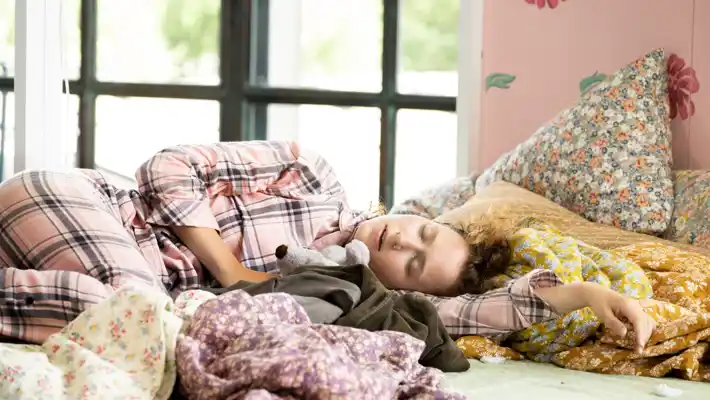 A woman in checkered pajamas lies in bed, sleeping.