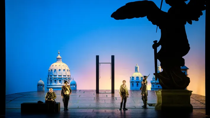 An open space with a hanging device, several soldiers and a lost man, in the background a blue sky and house facades.