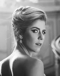 En närbild på en blond kvinna, ryggen vänd mot kameran, hon tittar över sin axel mot oss.