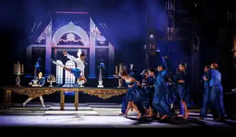 Runt ett stort bord rör sig flera personer: en man gör ett stort över bordet.