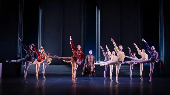 Flera män i vackra kostymer dansar i formation på en scen.