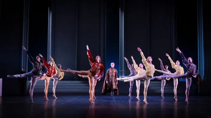 Several men in beautiful costumes dance in formation on a stage.