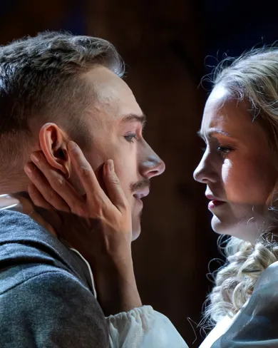 A man and a woman standing opposite each other, she holds her hand against his cheek.